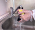 A person wearing gloves washing a kitchen faucet with a sponge, highlighting the ease of cleaning a fingerprint-resistant surface.