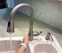 A hand activating a single handle kitchen faucet with a motion sensor, showcasing its convenience for messy cooking days.