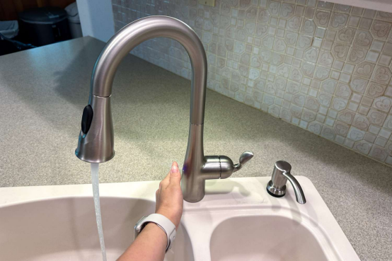 A hand activating a single handle kitchen faucet with a motion sensor, showcasing its convenience for messy cooking days.